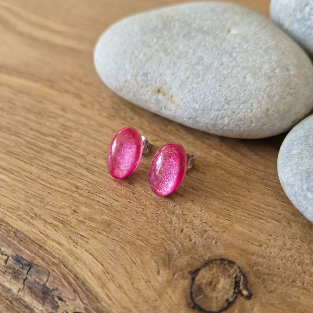 Pink oval earrings on a wooden surface with stones in the background