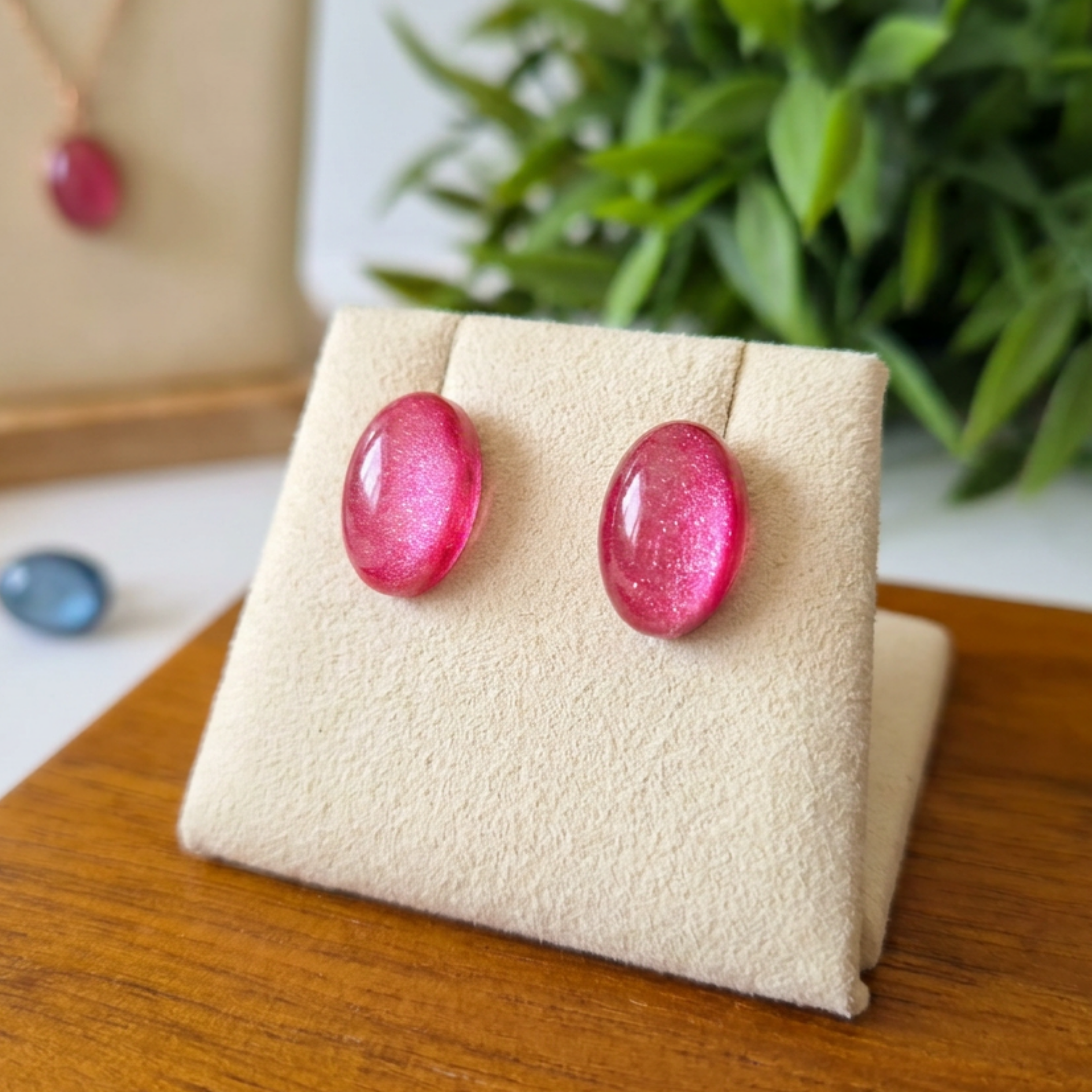 Pink earrings on a beige jewelry display with a blurred green plant in the background