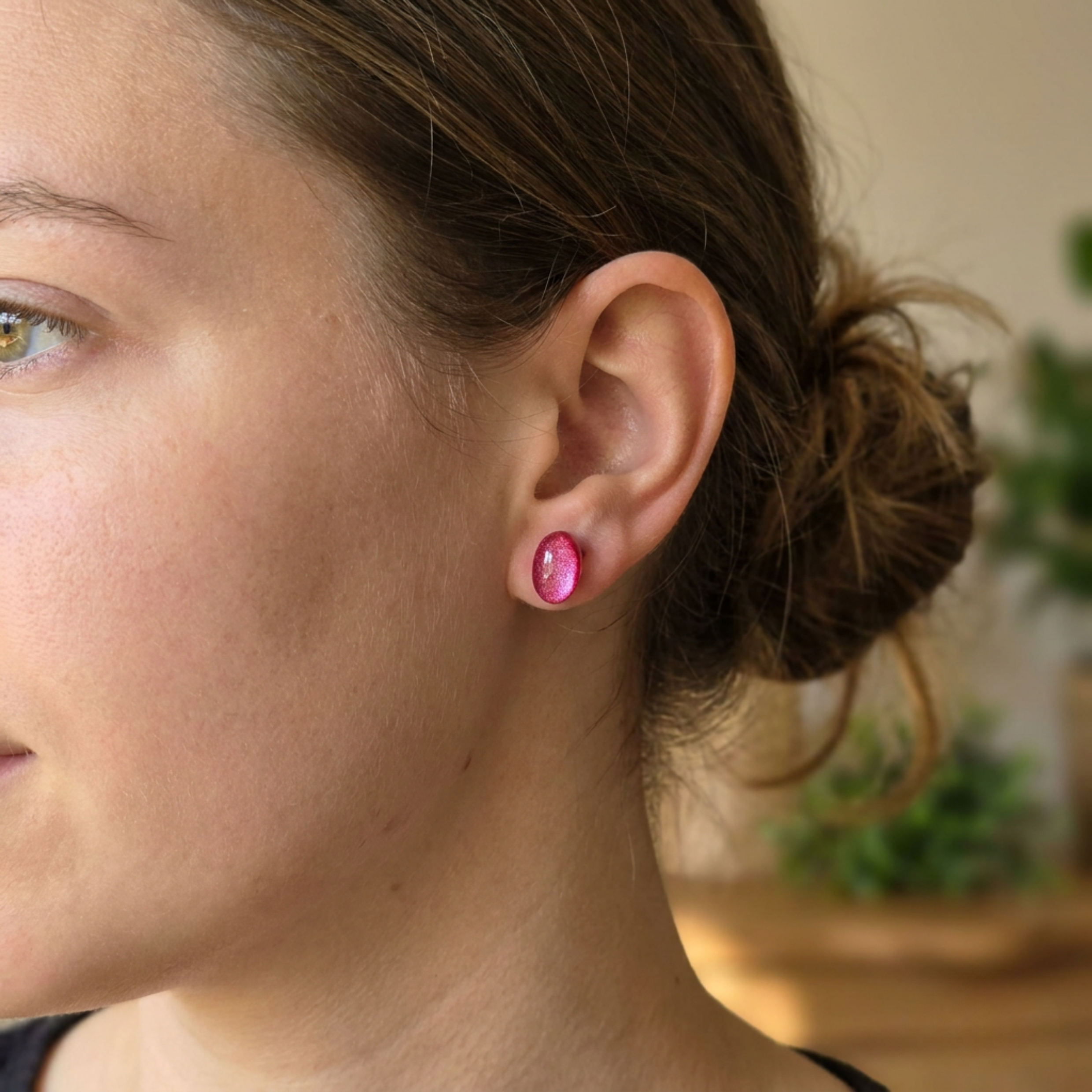 Close-up of a person wearing pink earrings with a blurred indoor background