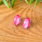 Pink earrings on a wooden surface with green leaves in the background