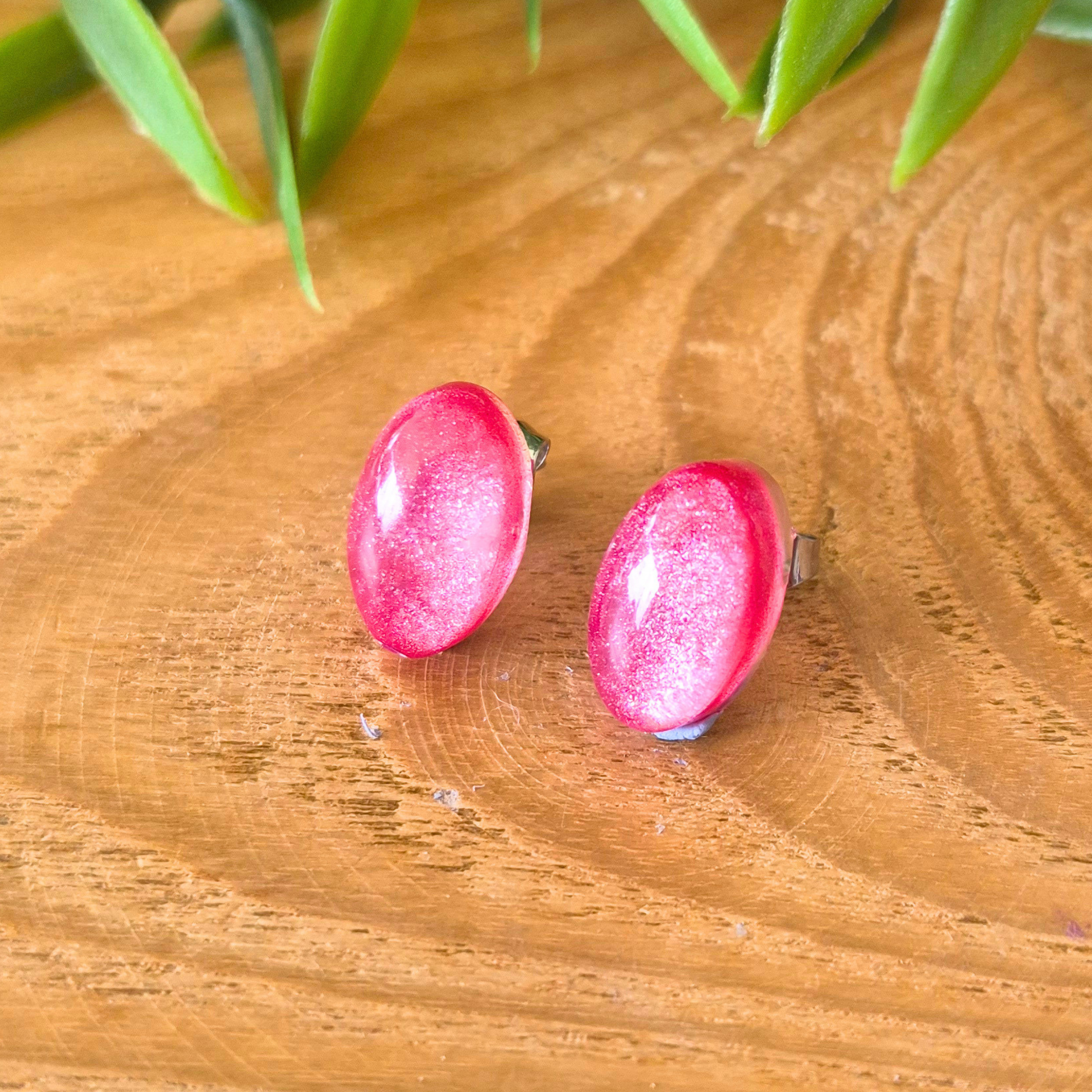 Pink earrings on a wooden surface with green leaves in the background