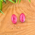 Pink oval earrings on a wooden surface with green leaves in the background
