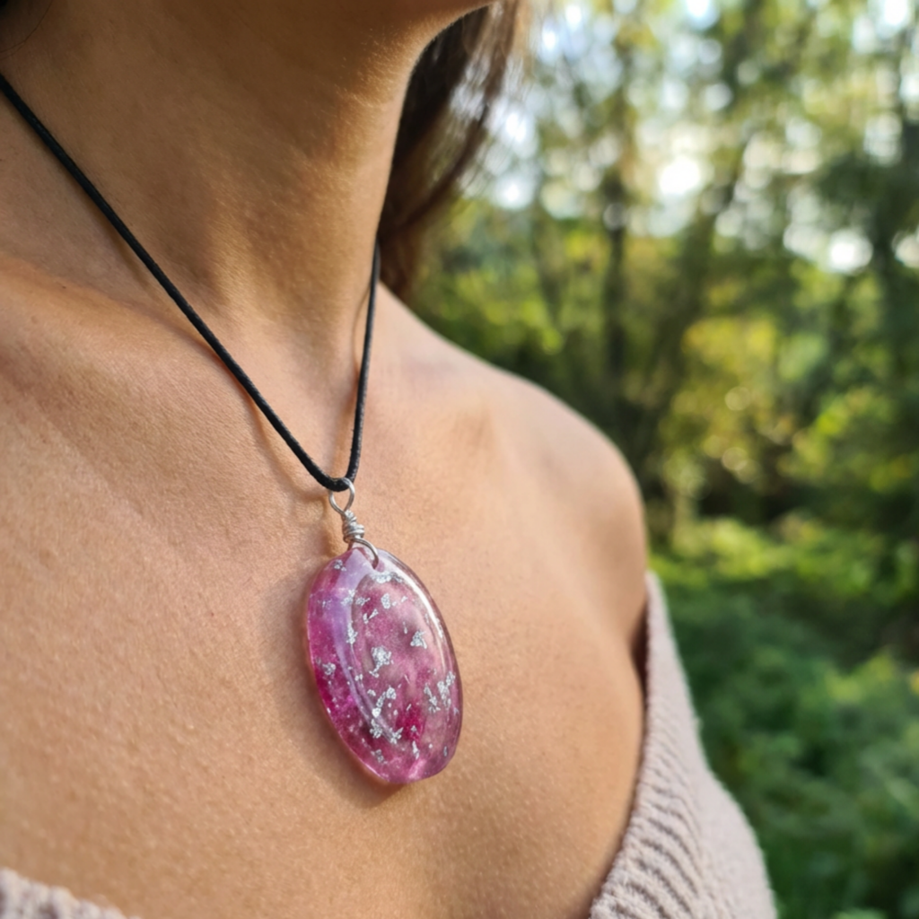 Person wearing a necklace with a pink teardrop pendant against a blurred green outdoor background