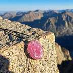 Pink stone pendant on a chain against a mountainous landscape