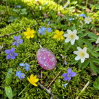 Pink pendant on a chain surrounded by colorful flowers on green moss