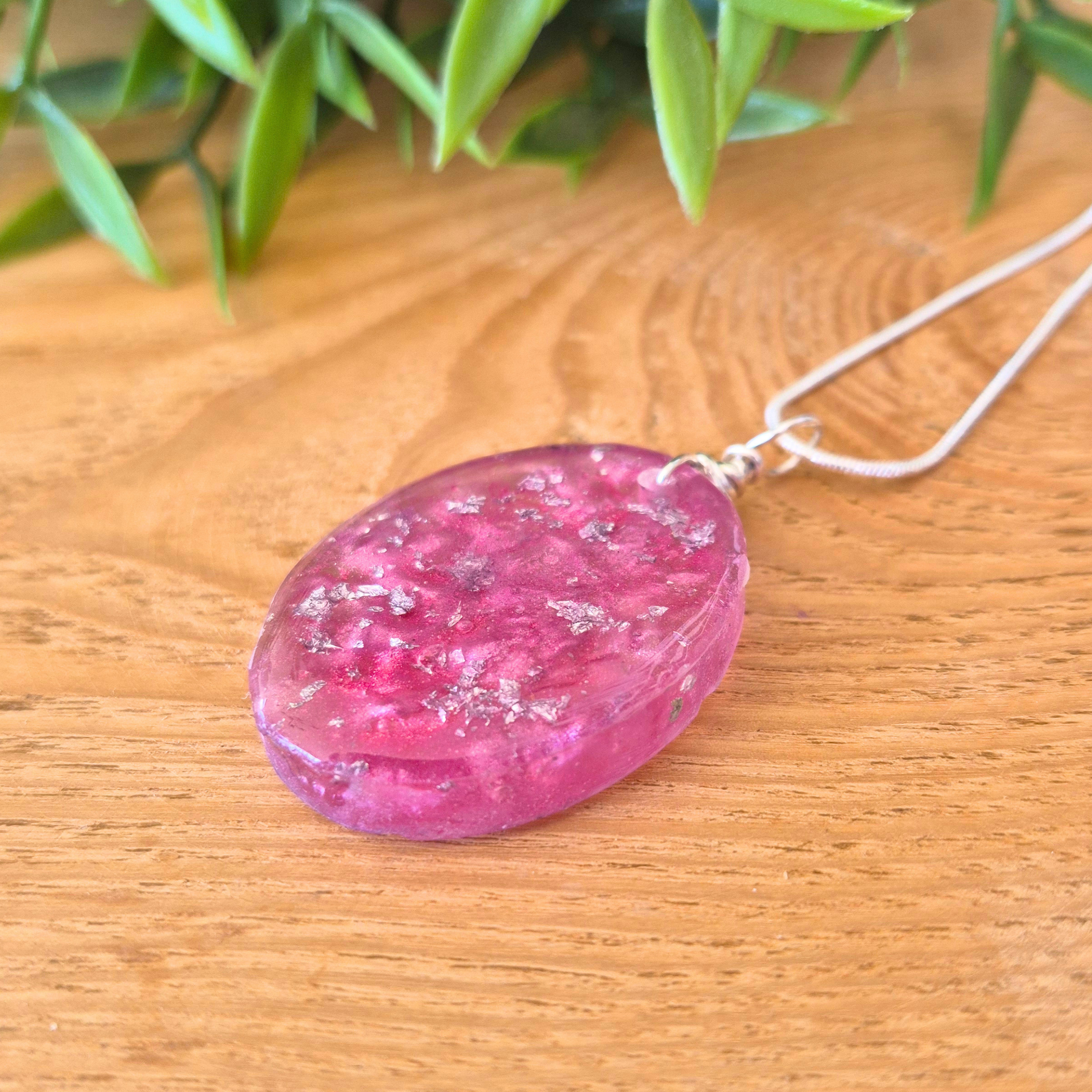 Pink oval pendant necklace on a wooden surface with green leaves in the background