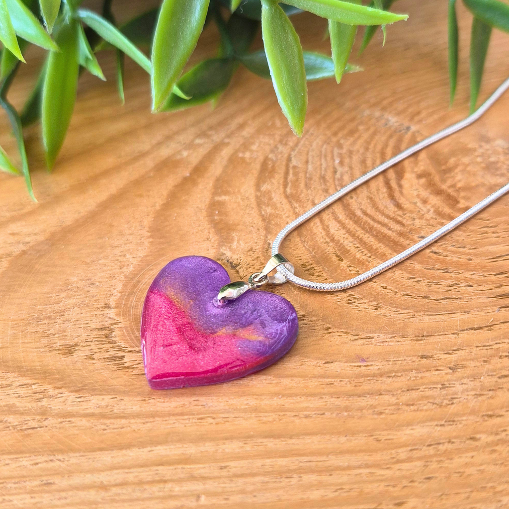 Dainty gold and purple heart on a silver bail and chain on a wooden surface