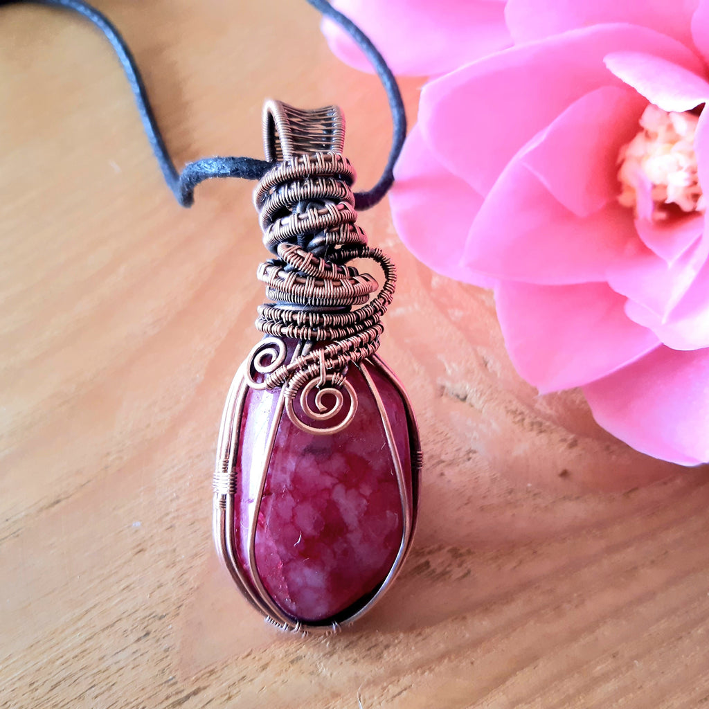 Pink pendant with wire wrapping on a wooden surface with a pink flower