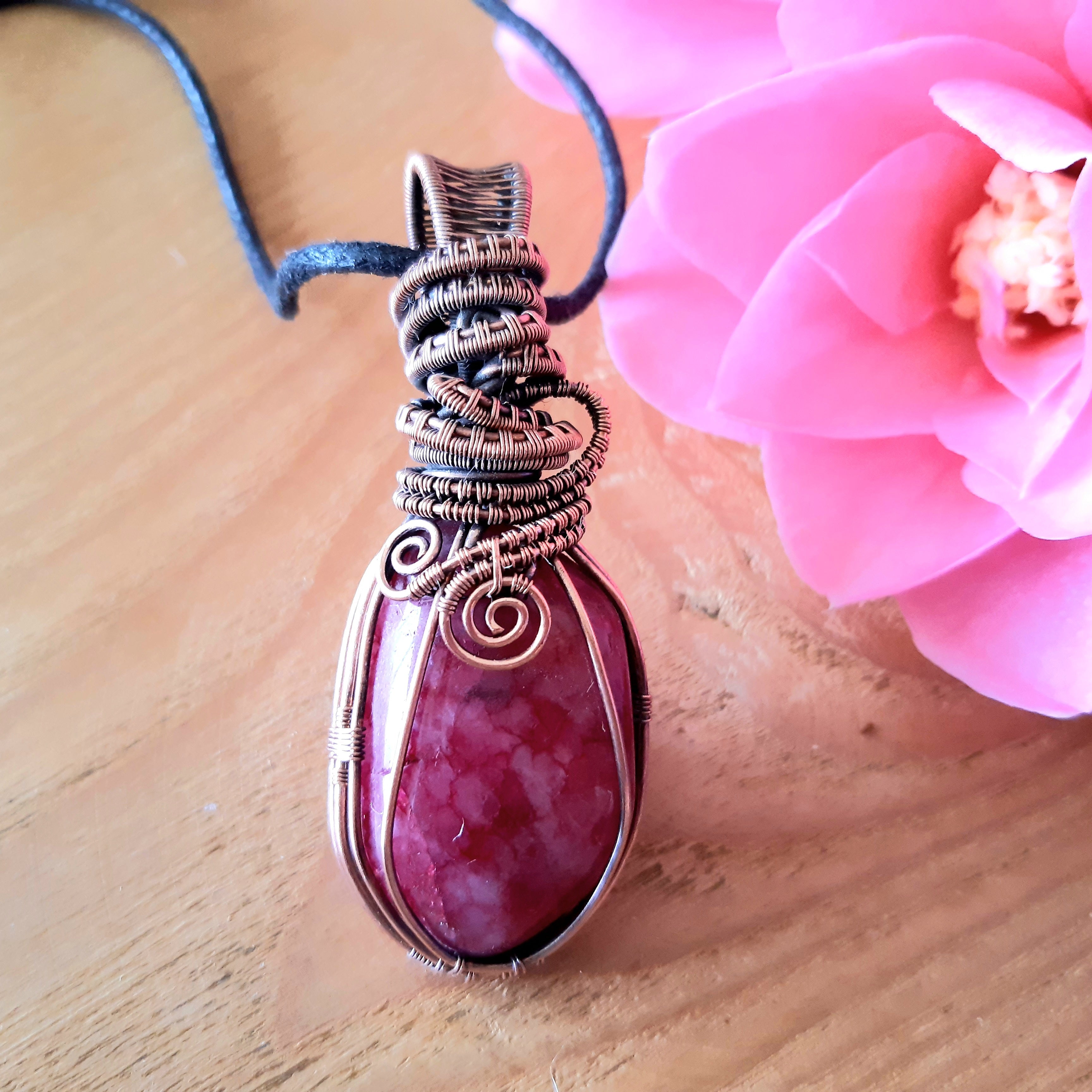 Pink pendant with wire wrapping on a wooden surface with a pink flower