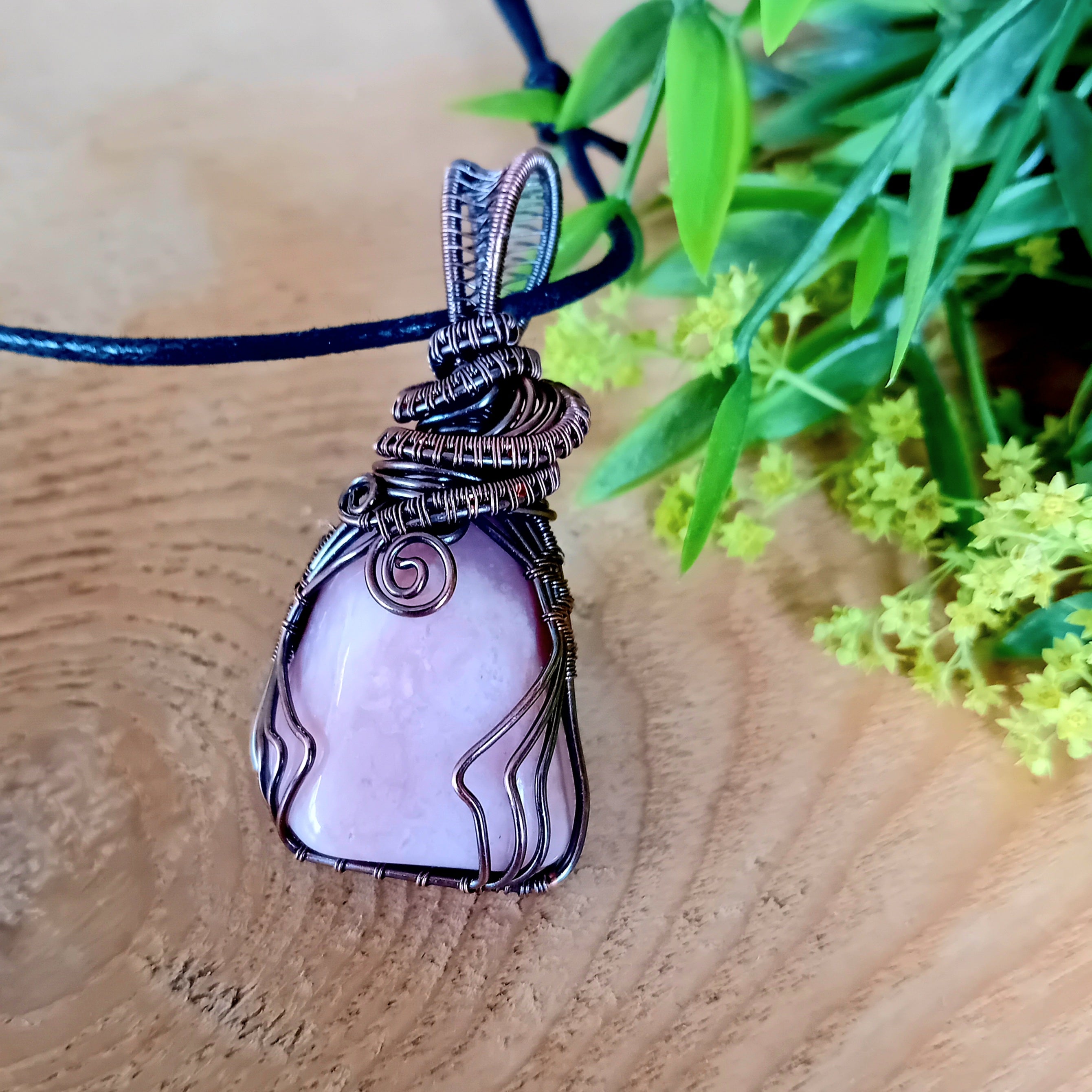 Pink stone pendant on a blue cord with greenery in the background
