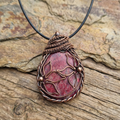 Rhodonite copper wire wrapped pendant with flowers on a stone and wood surface