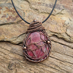 Rhodonite copper wire wrapped pendant with flowers on a stone and wood surface