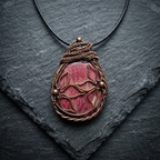 Copper wire wrapped pendant with a Rhodonite gemstone and copper wire flowers on a slate surface