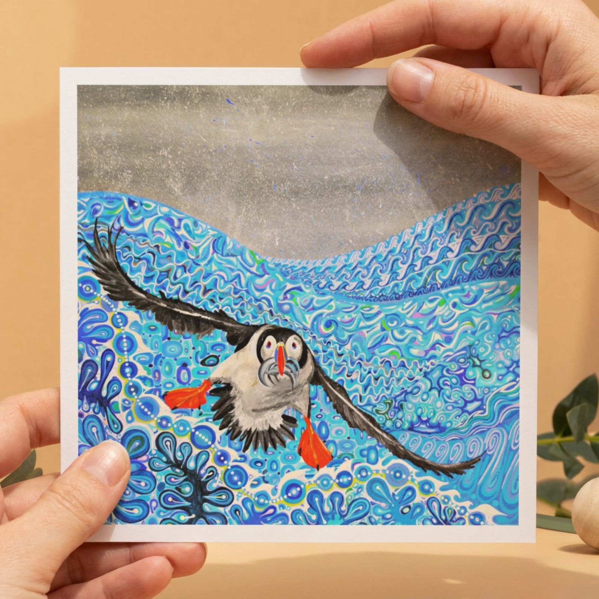 Hand holding a card with a colourful illustration of a puffin bird and fish underwater scene.