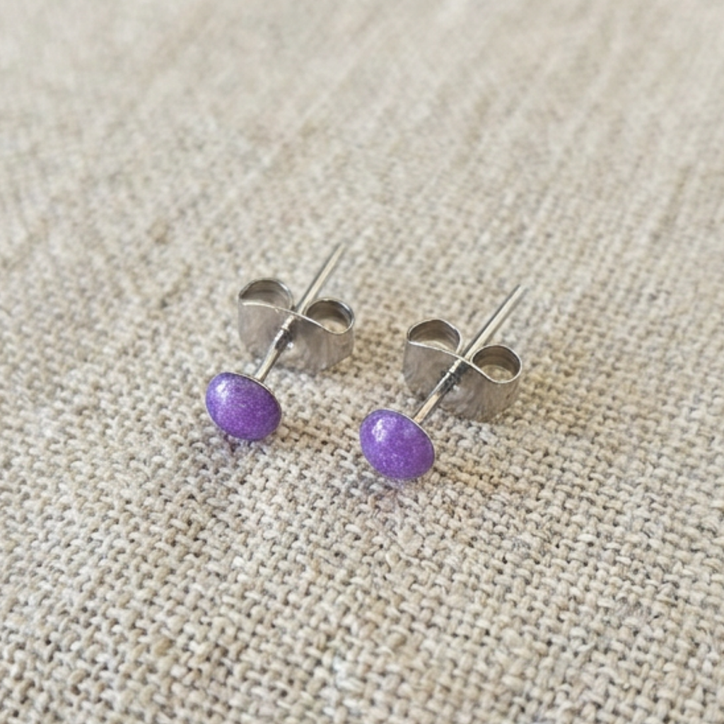 Pair of purple stud earrings on a beige fabric background