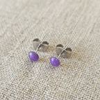 Pair of purple stud earrings on a beige fabric background