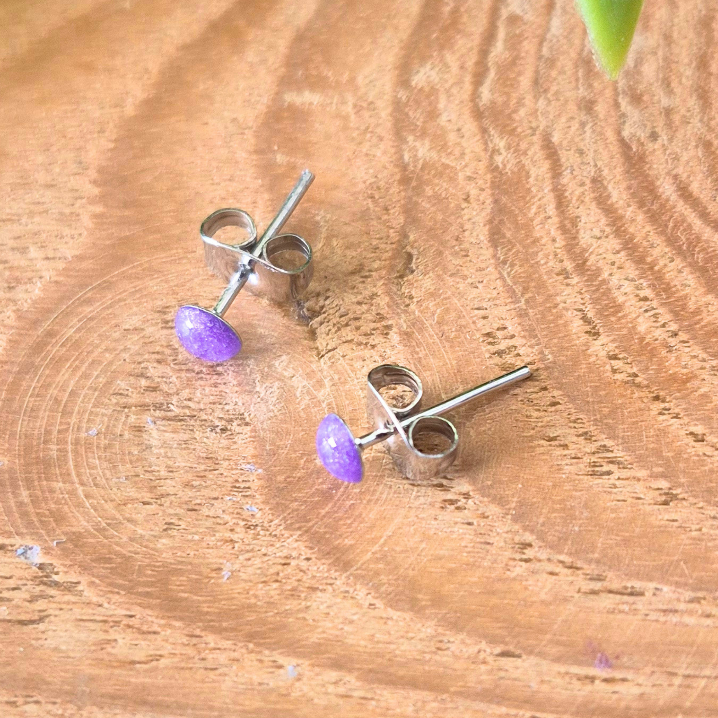 Pair of silver earrings with purple stones on a wooden surface