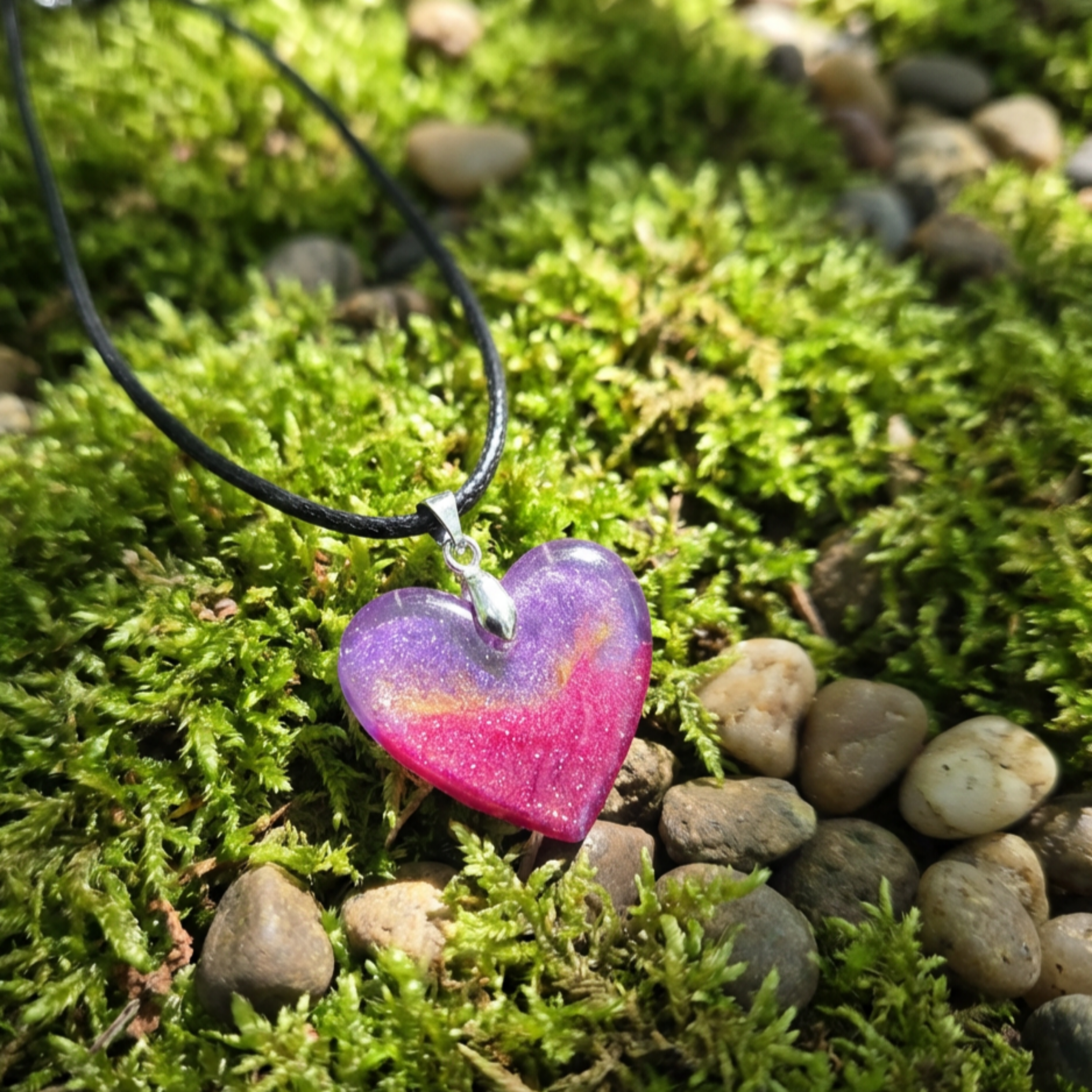 Small heart with purple gold and pink shimmers pendant on moss with pebbles