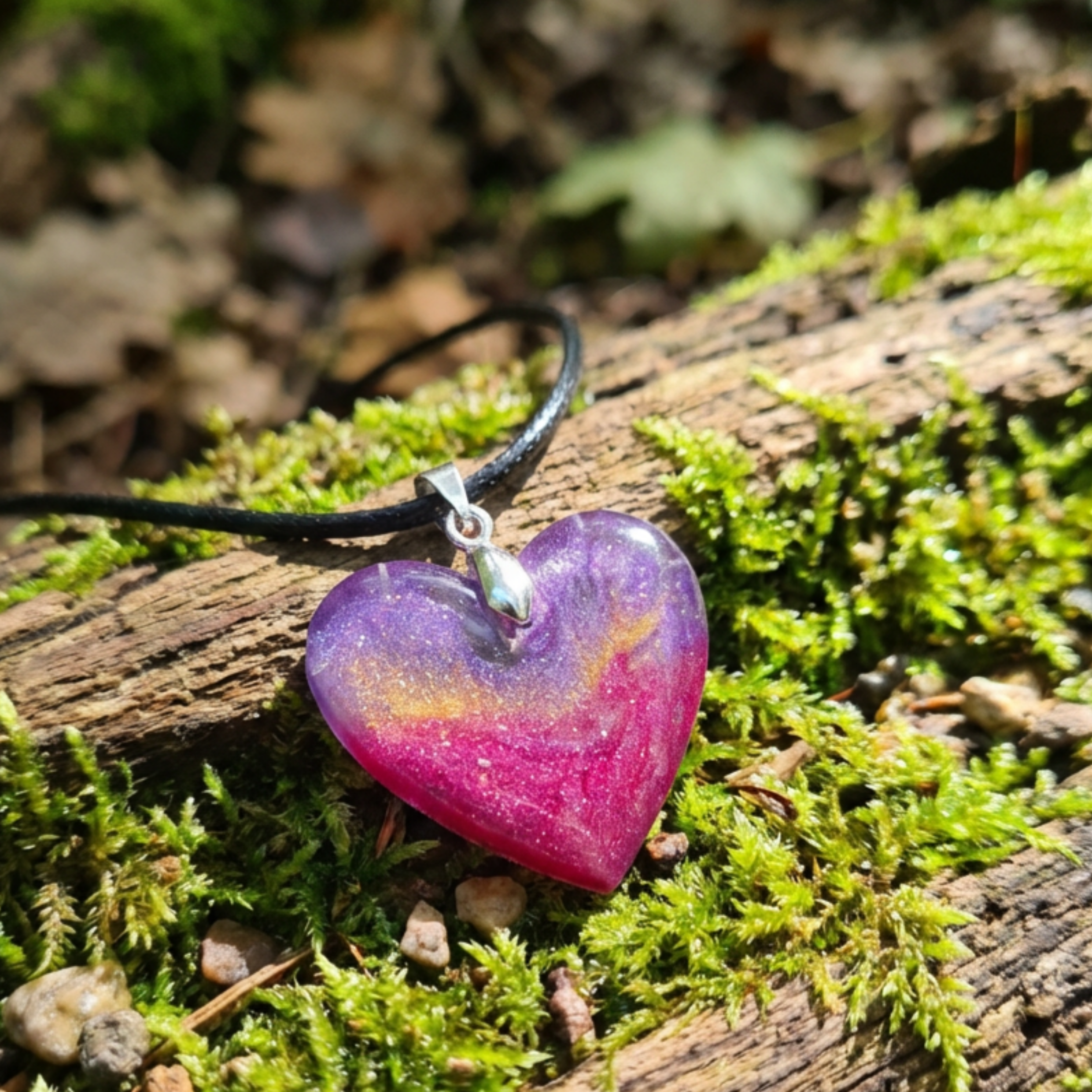 Heart-shaped purple and pink pendant on a black cord lying on a mossy log.