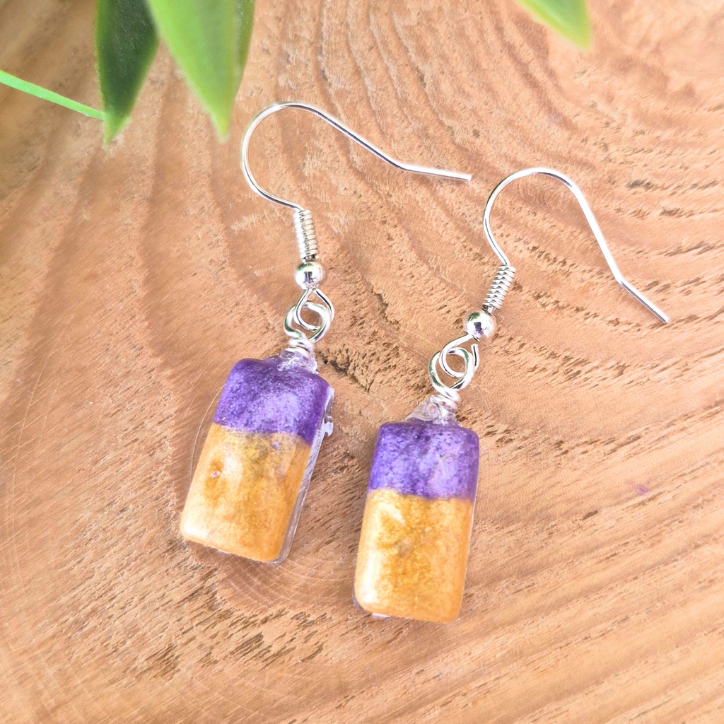 Pair of earrings with purple and orange beads on a wooden surface