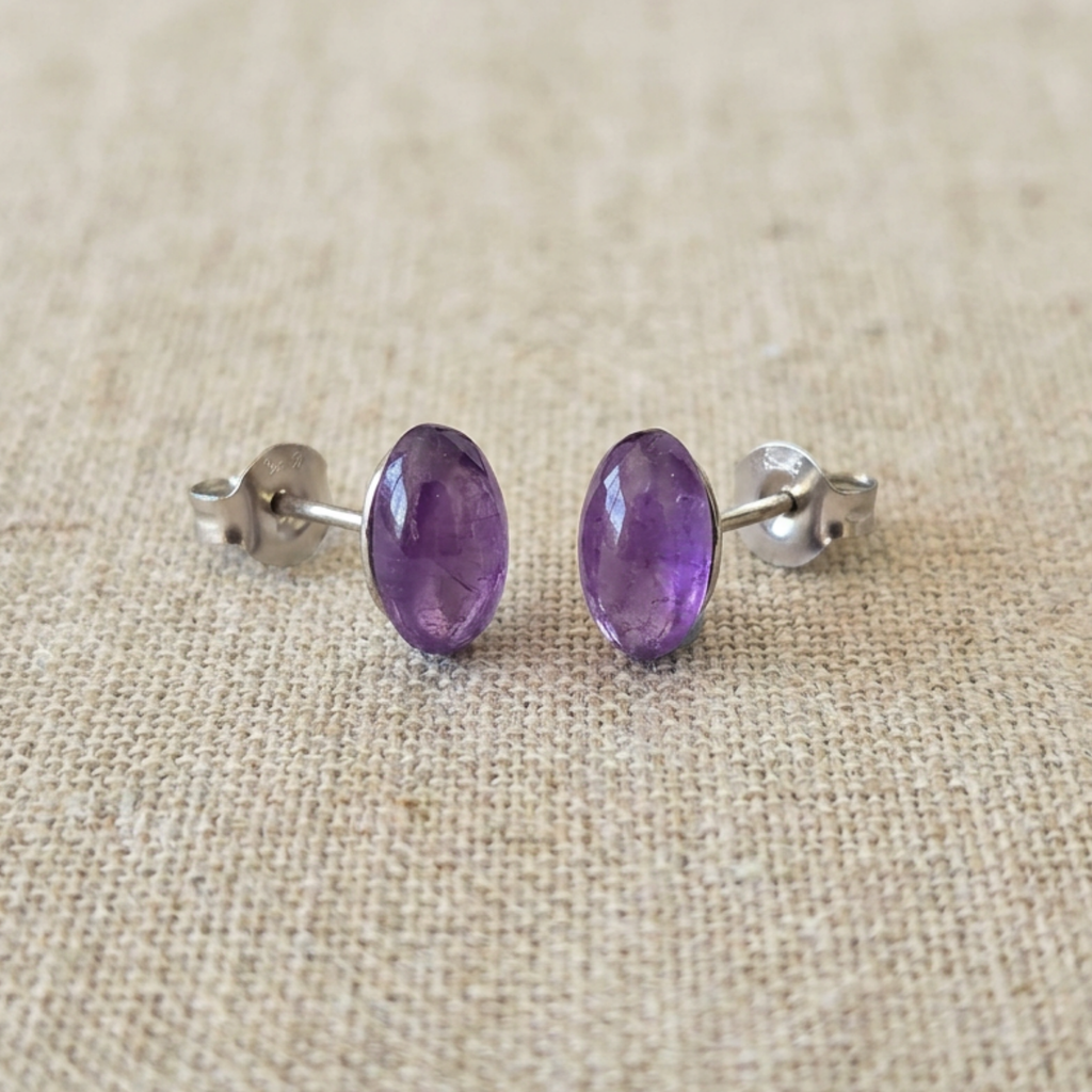 Pair of purple stud earrings on a beige fabric background