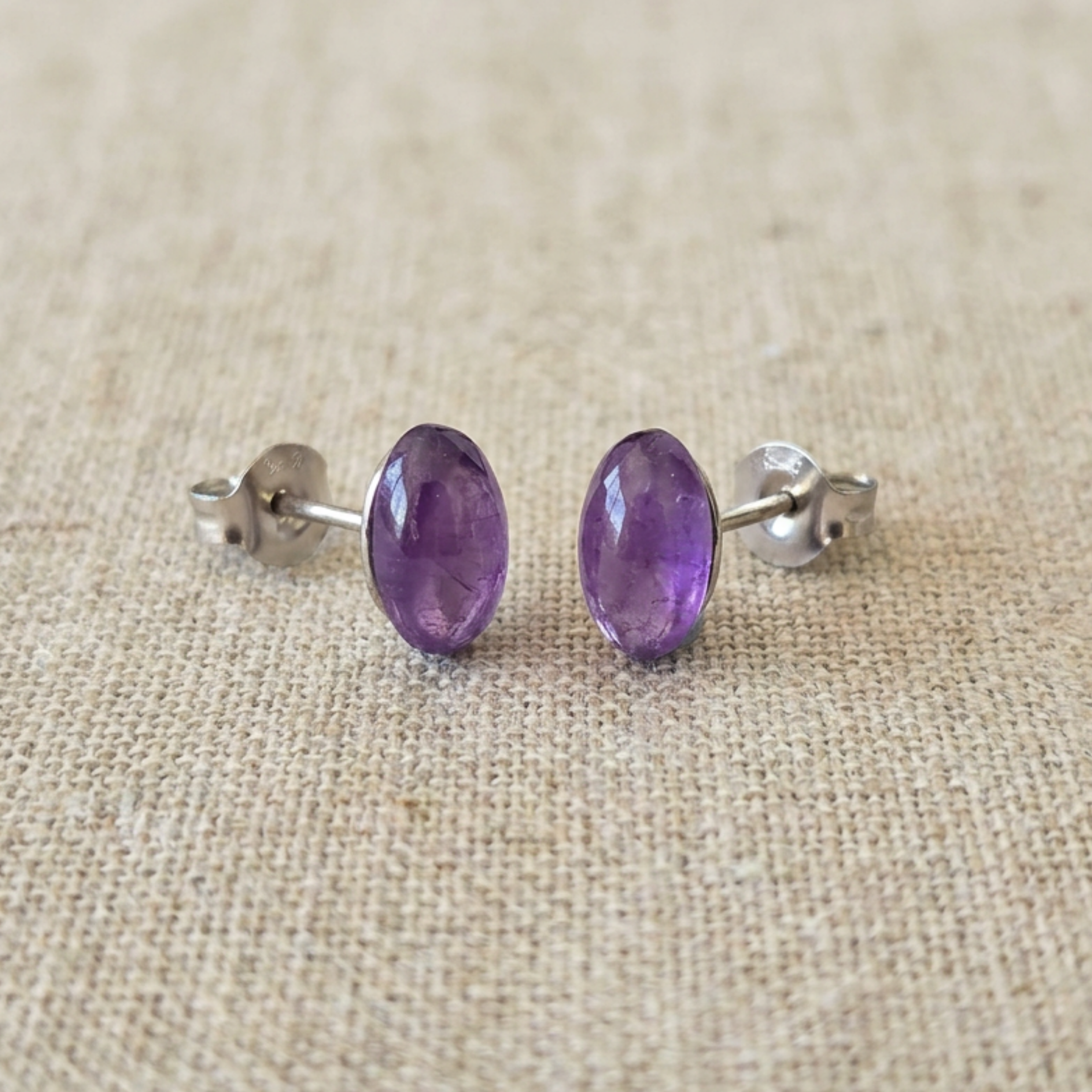 Pair of purple stud earrings on a beige fabric background