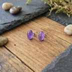 Purple gemstone earrings on a wooden surface with stones and moss in the background