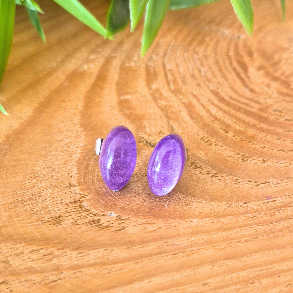Purple oval earrings on a wooden surface with green leaves in the background