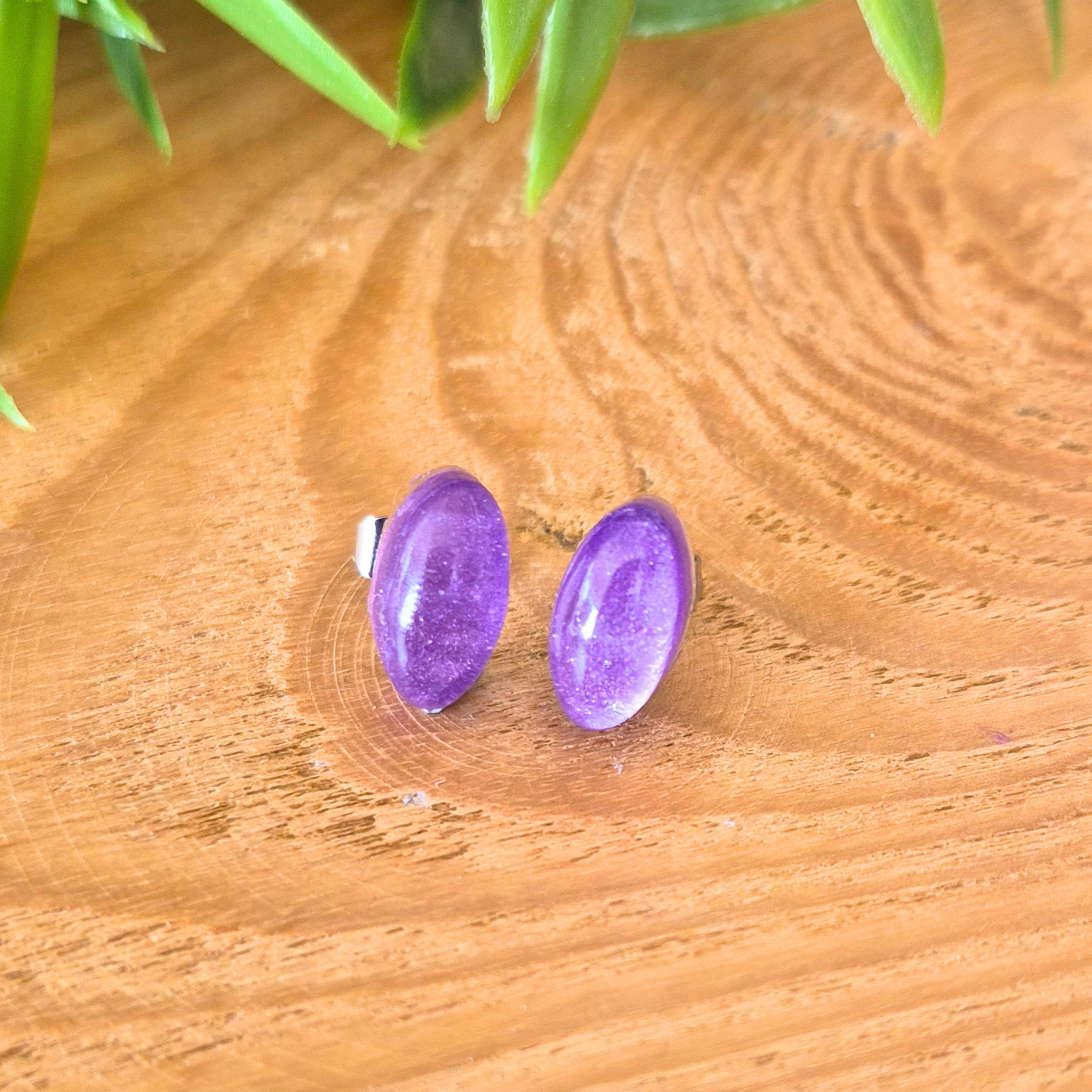Purple oval earrings on a wooden surface with green leaves in the background