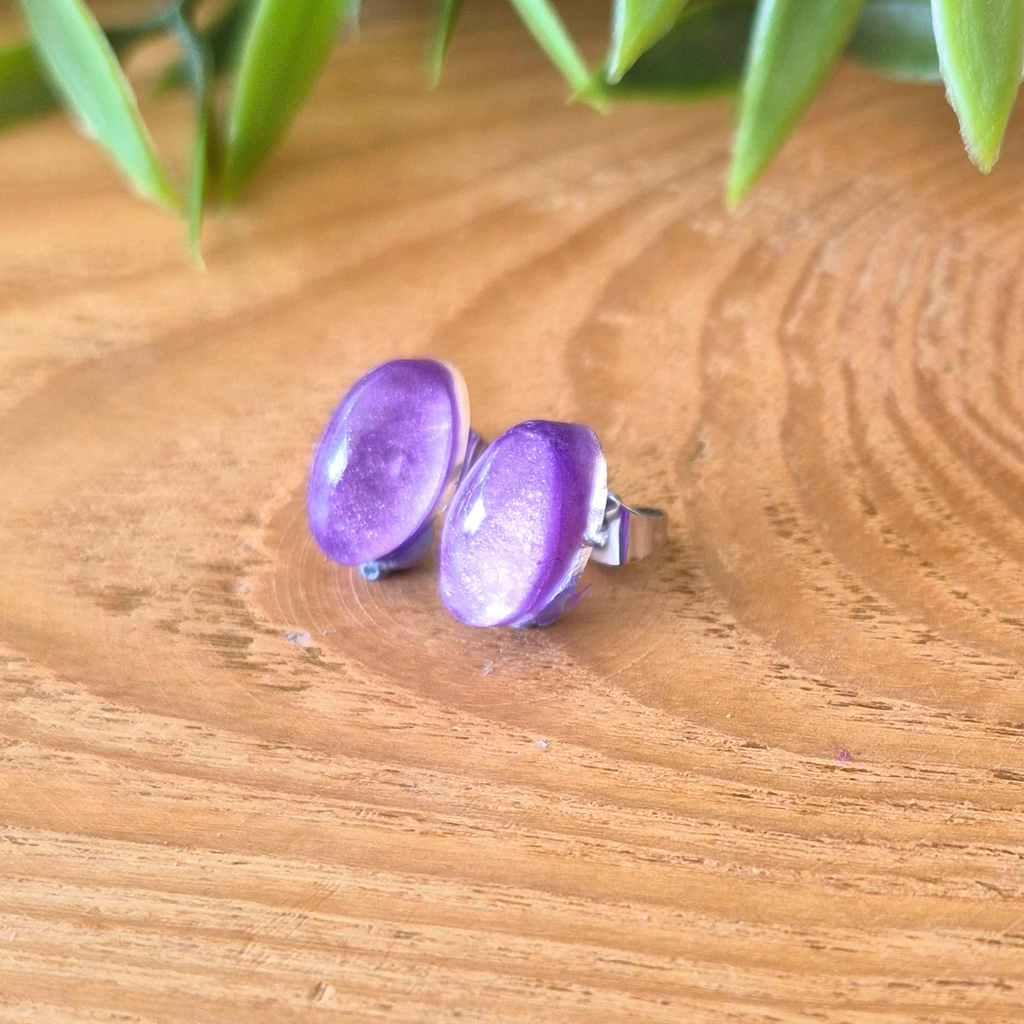 Purple stud earrings on a wooden surface with green leaves in the background