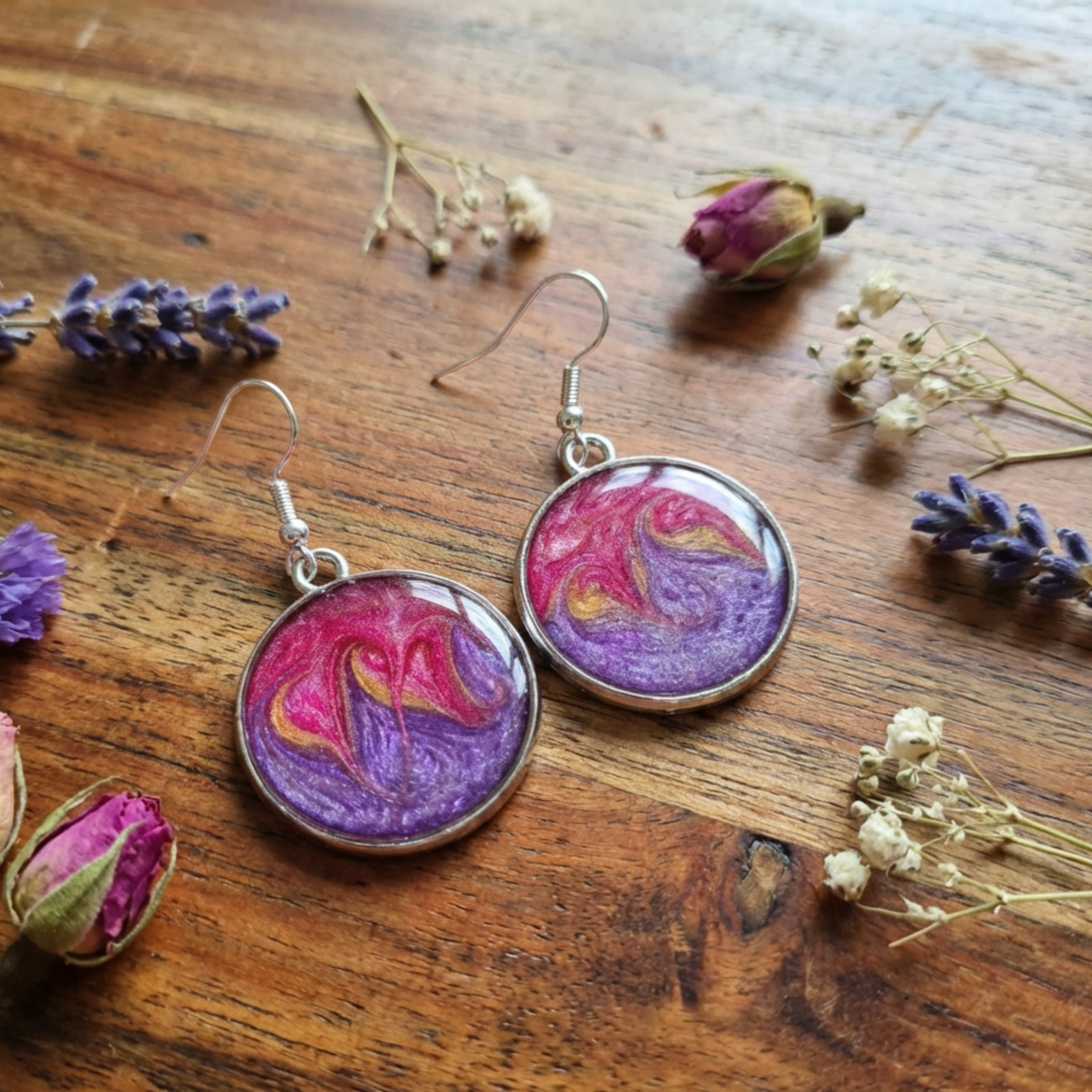 Pair of earrings with a purple and pink design on a wooden surface with lavender flowers.