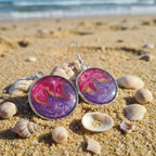 Purple and pink earrings on a sandy beach with shells
