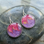 Pair of earrings with purple and pink marbled design on a stone surface