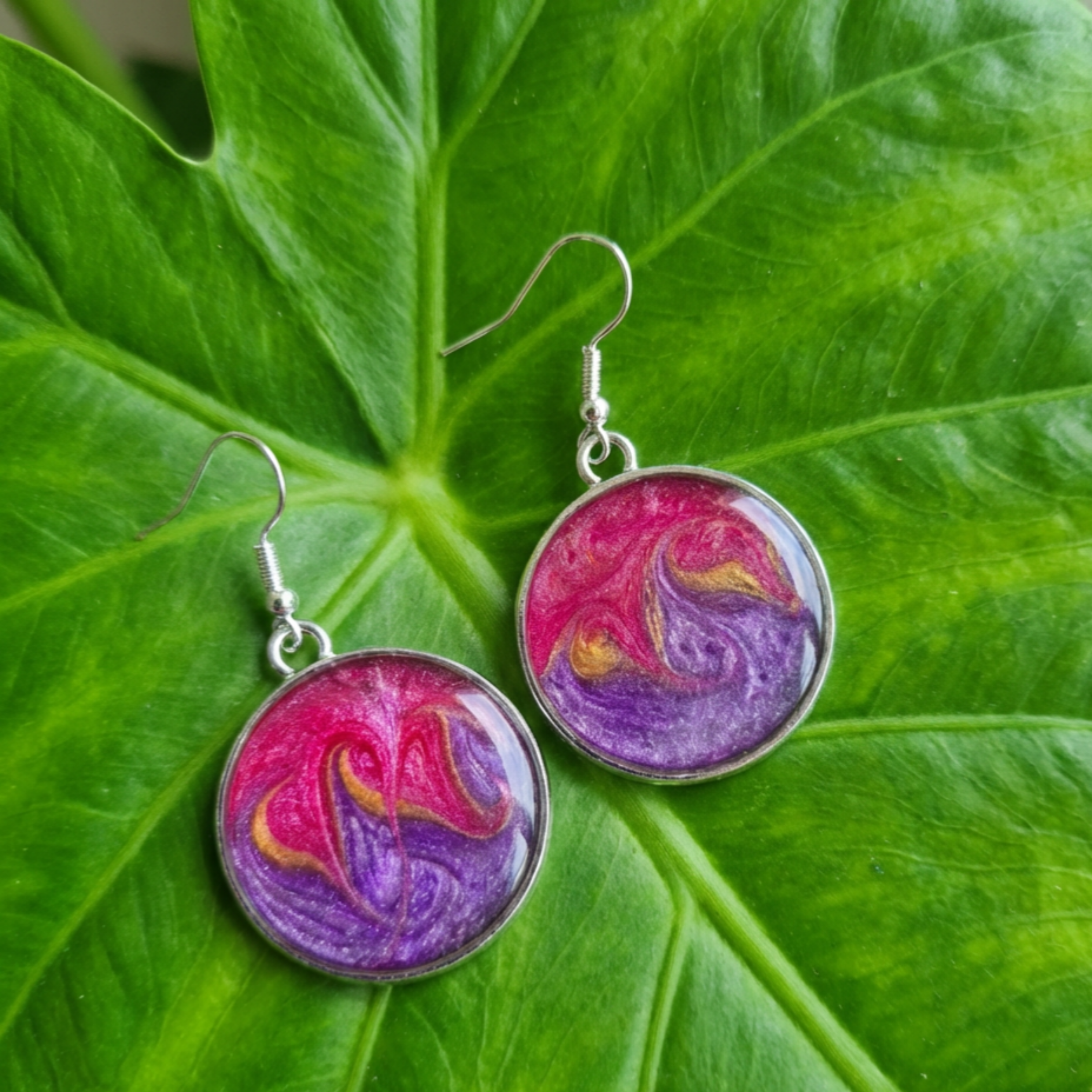 Pair of earrings with pink and purple designs on a green leaf background