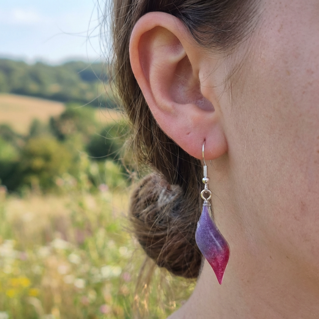 Close-up of an ear wearing a purple teardrop earring with a blurred natural background