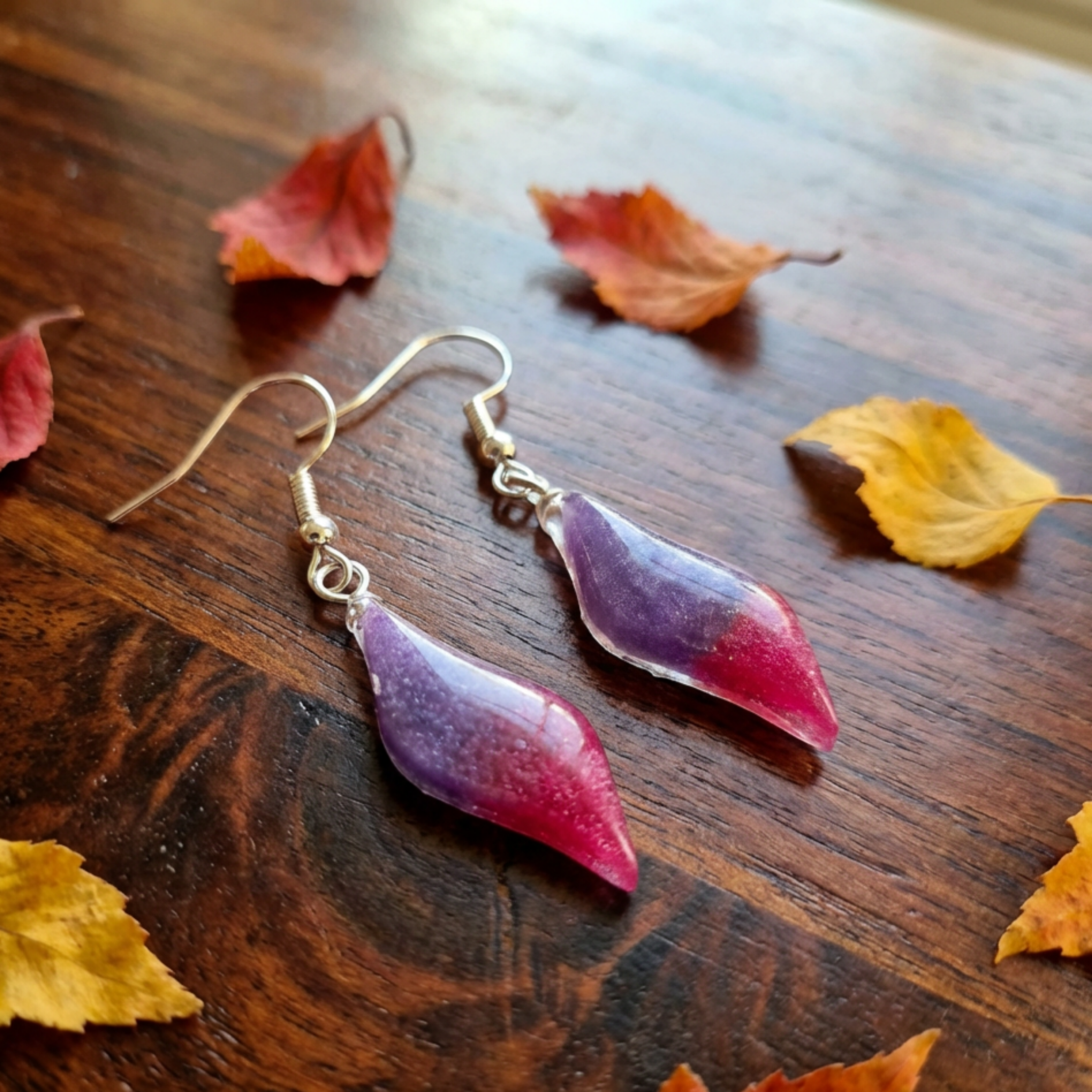 Purple and pink resin wavey earrings on ear wires on a wood table