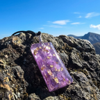 Purple pendant with gold accents on a rocky surface with a mountainous background