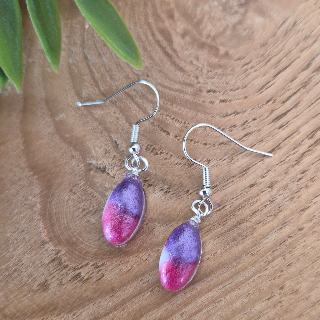 Purple and pink teardrop earrings on a wooden surface with green leaves.