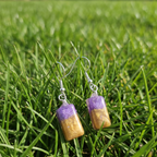 Dainty purple and gold rectangle drop earrings sitting in the grass