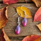 Purple and pink teardrop earrings on a wooden surface with autumn leaves.