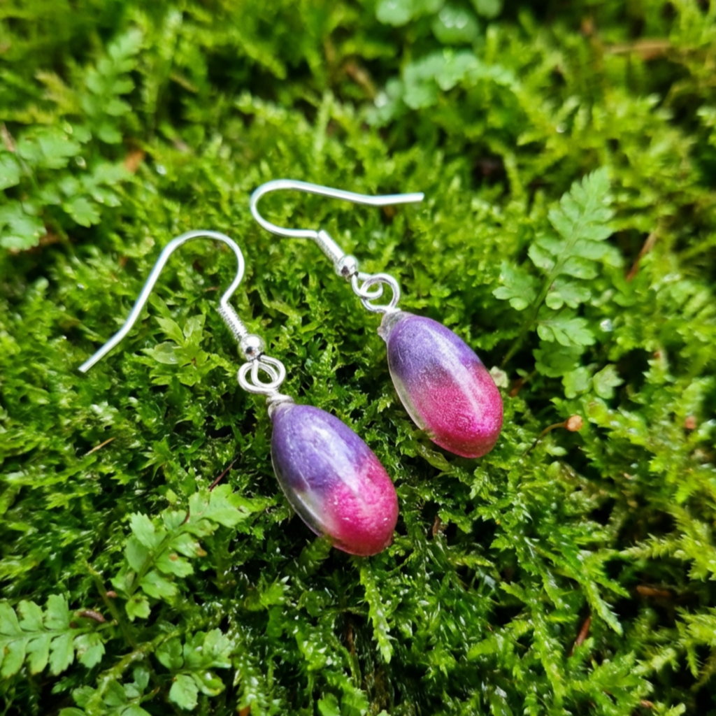 Purple and pink teardrop earrings on a green moss background