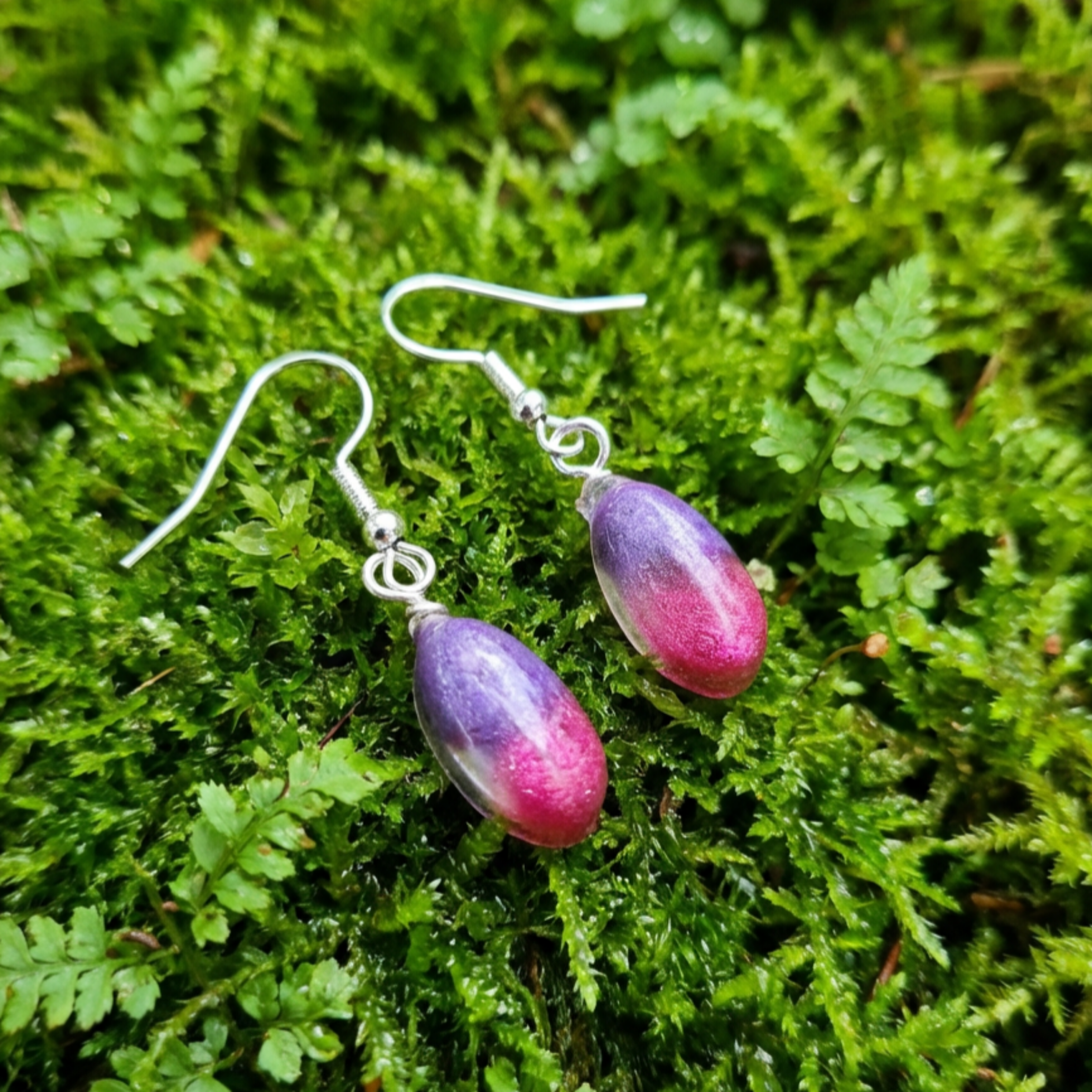 Purple and pink teardrop earrings on a green moss background