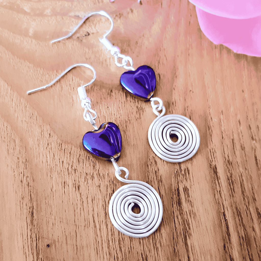 Earrings with purple heart and silver spiral designs on a wooden surface