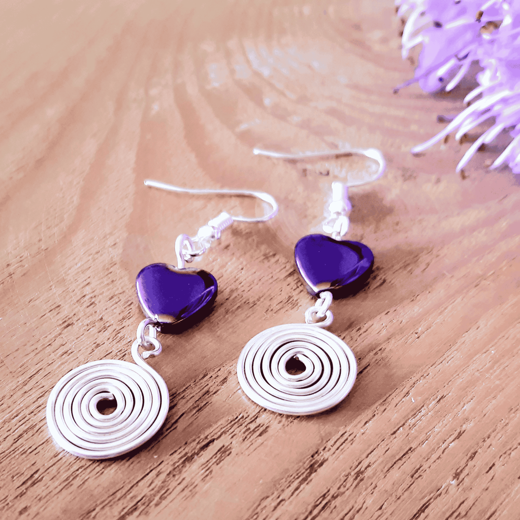 Earrings with purple heart charms and silver spiral designs on a wooden surface.