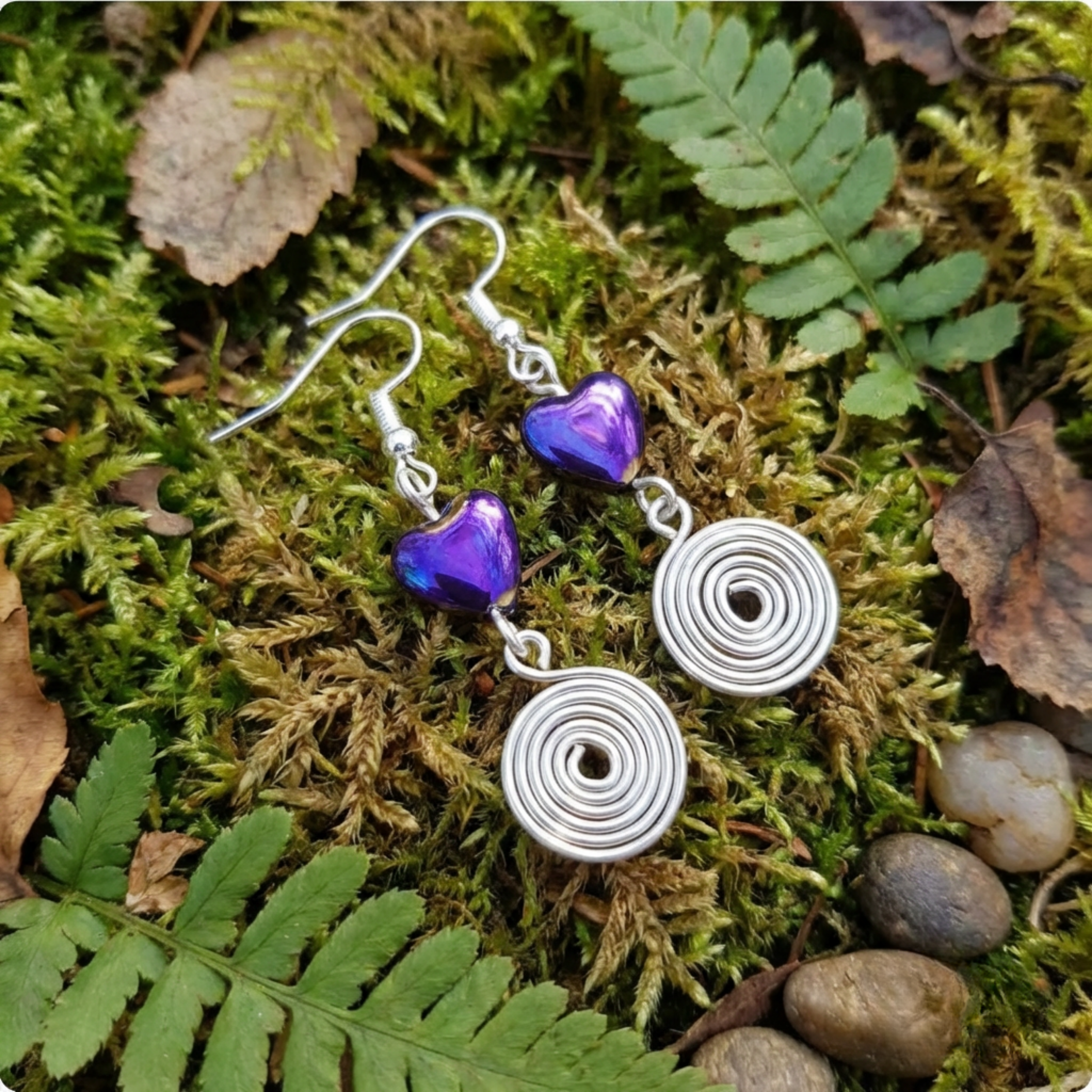 Silver earrings with purple heart beads on a mossy surface