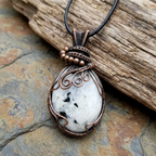 Pendant necklace with white stone and copper wire wrapping on a stone surface