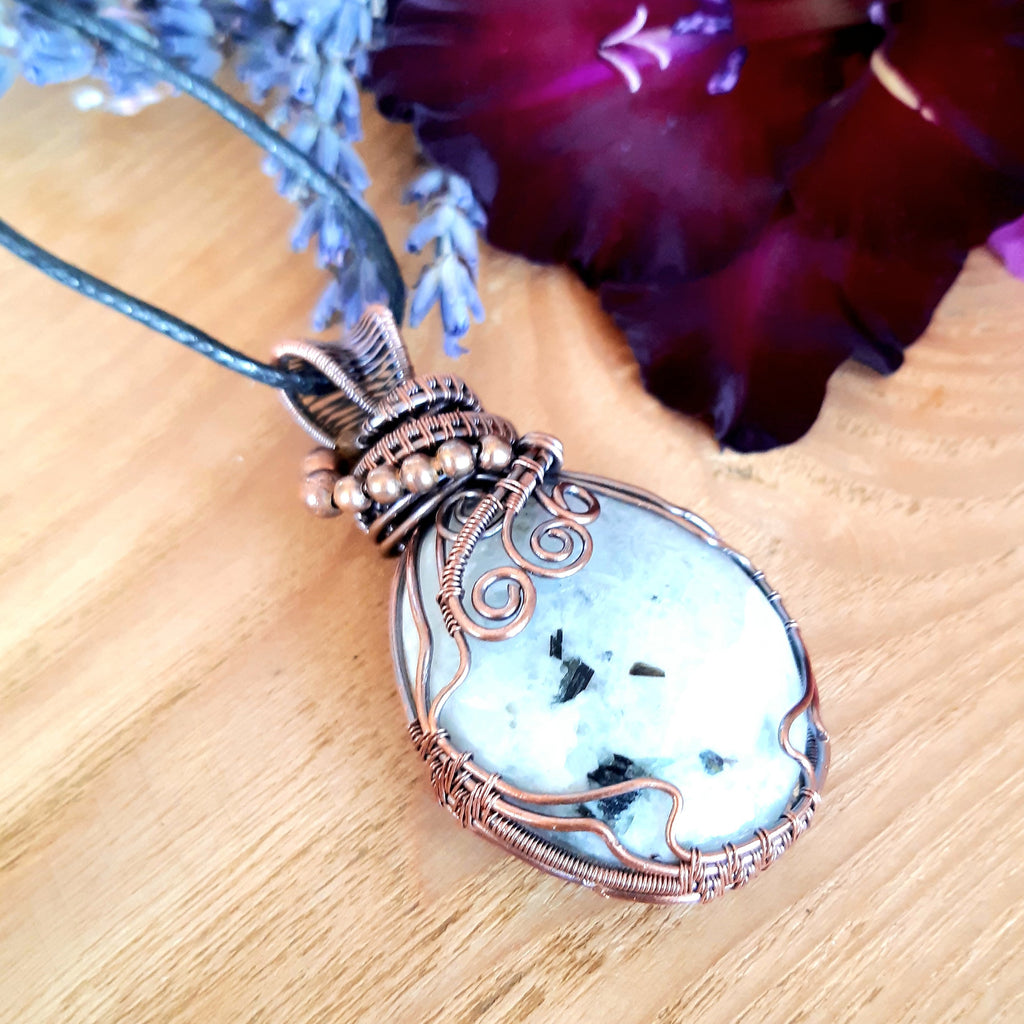 Necklace with a decorative pendant on a wooden surface with flowers in the background