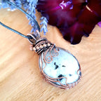 Necklace with a decorative pendant on a wooden surface with flowers in the background