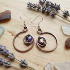 Copper hoop earrings with heart-shaped gemstones on a wooden surface with lavender flowers.