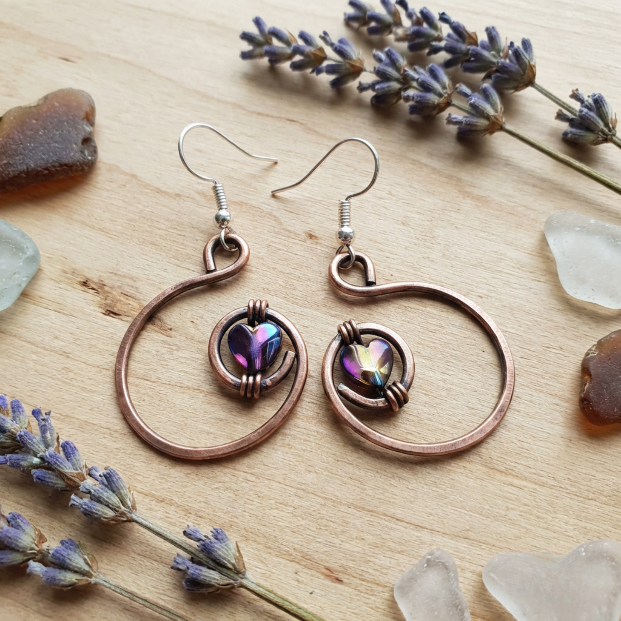 Copper hoop earrings with heart-shaped gemstones on a wooden surface with lavender flowers.